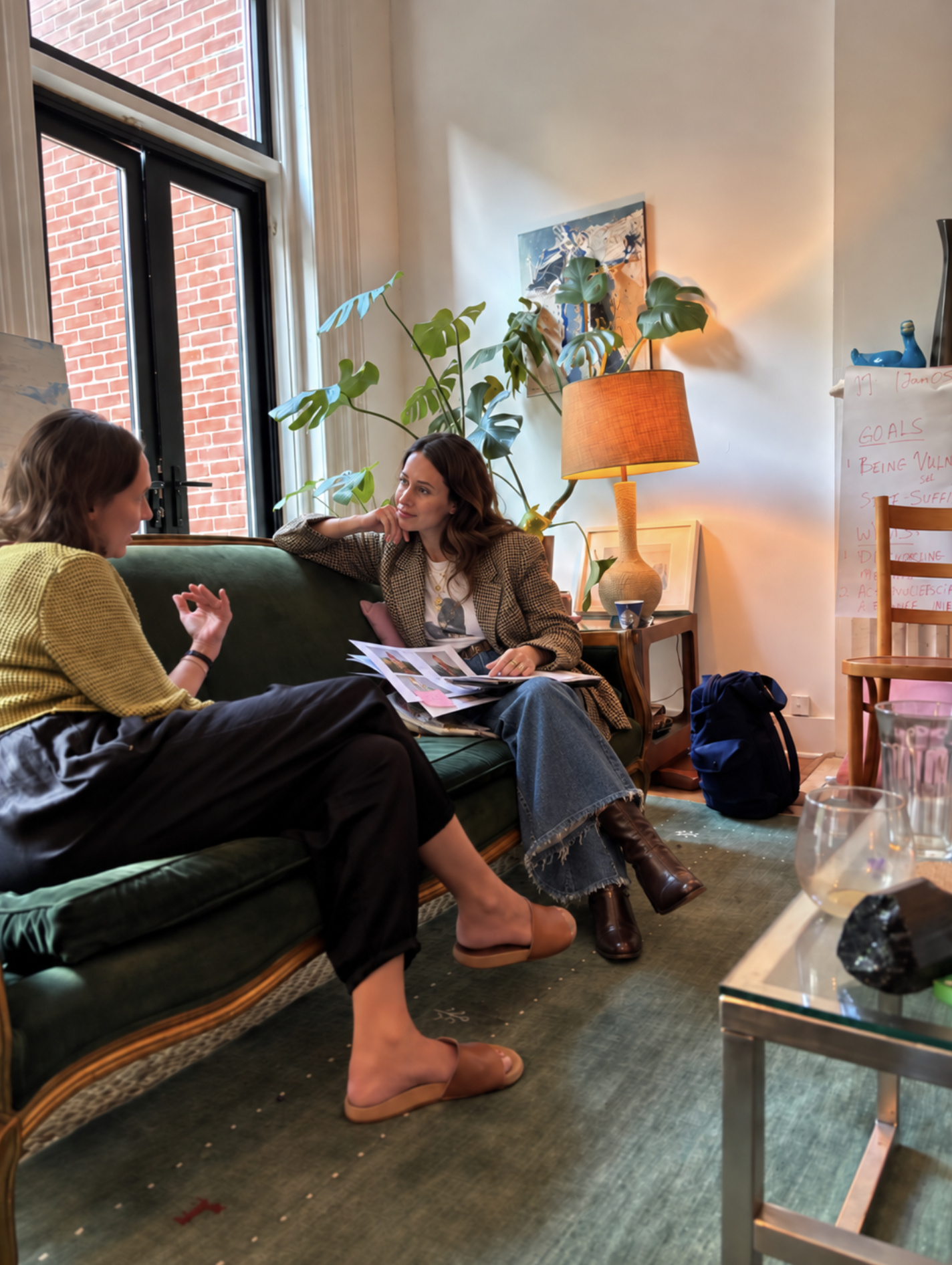 Two women in conversation on a green sofa in a sunlit room