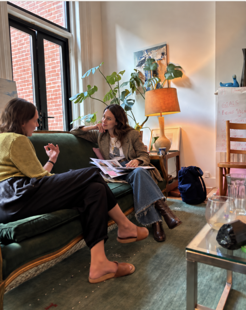 Two women in conversation on a green velvet sofa in a sunlit room